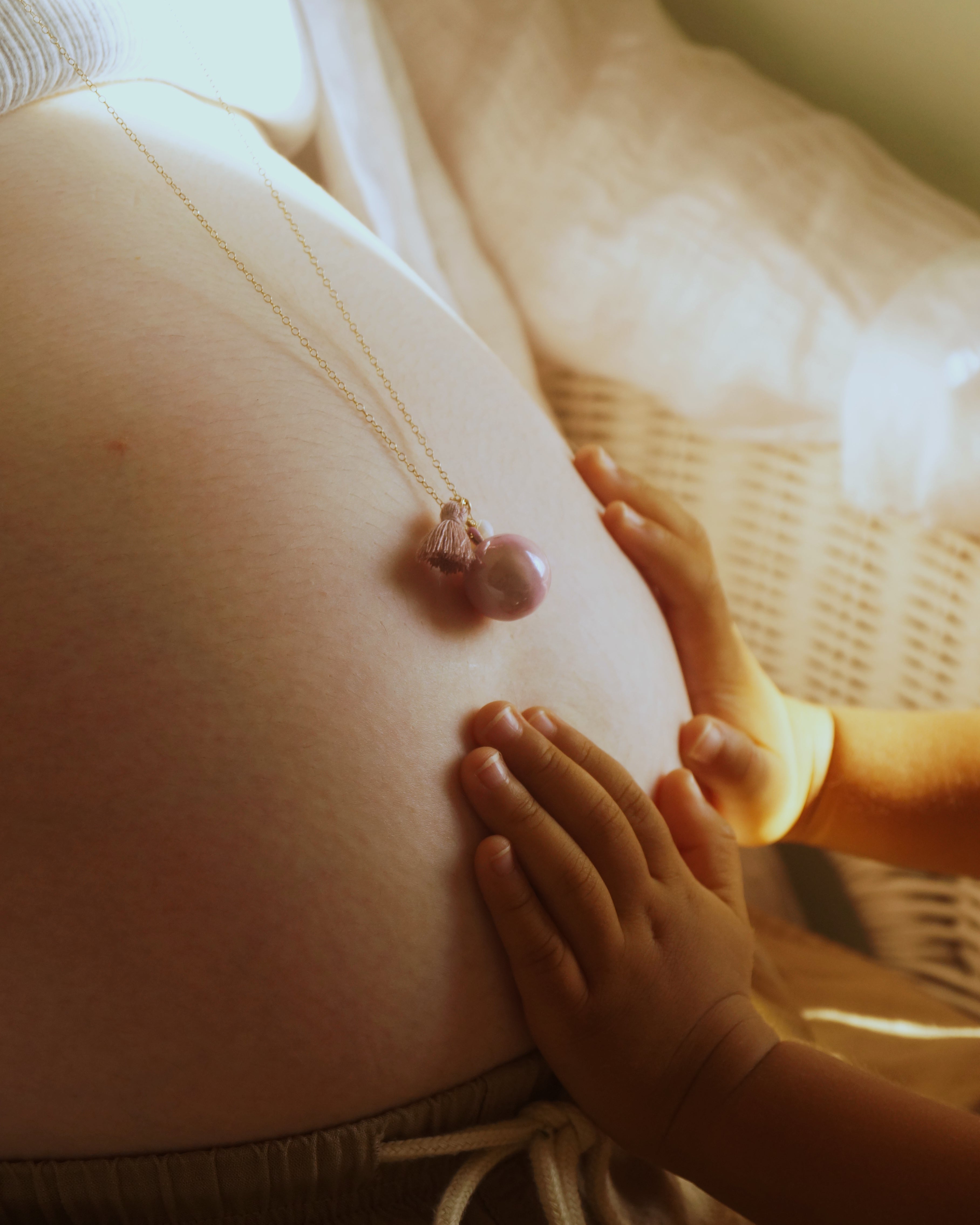 妊婦の女性がBo-emeブランドのマタニティネックレスを身につけ、赤ちゃんの小さな手が優しくお腹に触れる写真。胎教、安産祈願（anzan no omamori）、妊娠中のリラックス、プレママアクセサリー、ベビーシャワーギフト、妊婦ファッション、ヨガ・プレナタル、赤ちゃんをお腹で感じる方法など、妊娠期のさまざまなテーマに対応した画像です。妊娠中のスキンケアや栄養管理、出産準備を進める妊婦の生活には、マタニティウェアや妊婦帯、妊婦マークや母子健康手帳が欠かせません。胎教や安産祈願のために、胎教ネックレス、安産祈願ネックレス、お守りネックレスを身につけ、ガムランボールやハーモニーボールで穏やかな胎動を感じましょう。