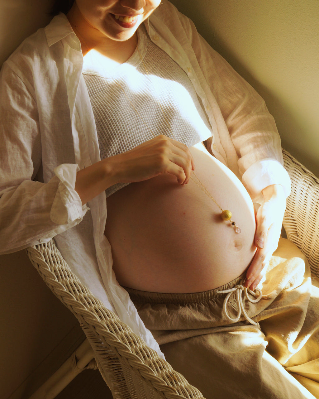 Boemeのマタニティネックレスを着けた妊婦の写真。赤ちゃんの手がお腹に触れ、胎教、安産祈願（anzan no omamori）、プレナタルヨガ、妊婦リラックス、ベビーシャワーや出産祝いギフトに最適なシーンです。胎教、安産祈願（anzan no omamori）、妊婦ファッション、ヨガ・プレナタル、ベビーシャワーギフト、妊娠報告にも最適です。出産準備に必要な妊娠中の食事や栄養、スキンケアを整えながら、妊娠報告や胎動を楽しむ妊婦。マタニティウェアや妊婦帯、妊婦マーク、母子健康手帳は必須。胎教ネックレス、安産祈願ネックレス、お守りネックレスに加え、ガムランボールやハーモニーボールを活用して、胎教と安産祈願を両立させましょう。