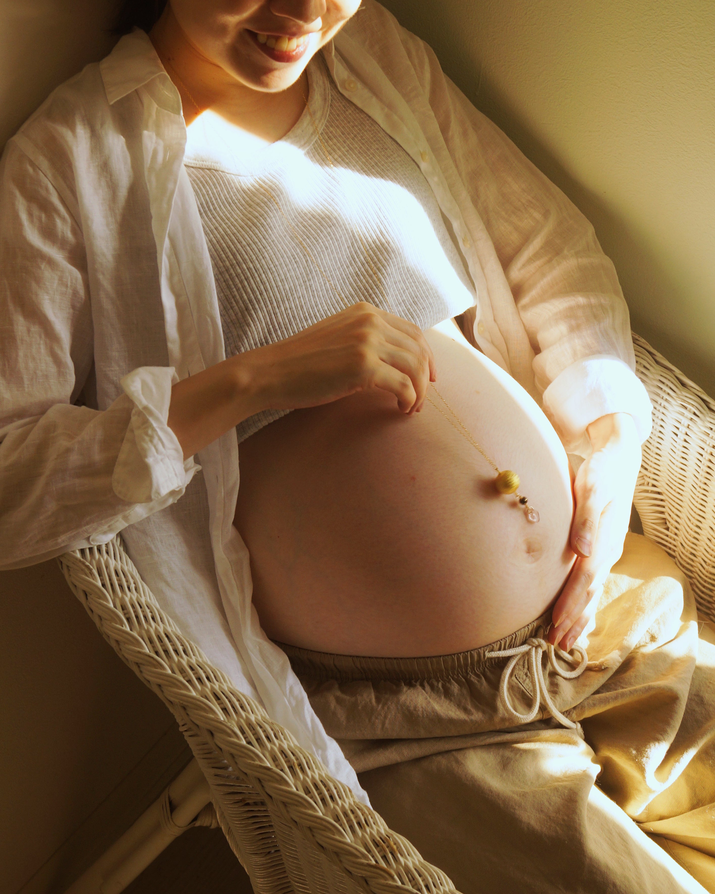 Boemeのマタニティネックレスを着けた妊婦の写真。赤ちゃんの手がお腹に触れ、胎教、安産祈願（anzan no omamori）、プレナタルヨガ、妊婦リラックス、ベビーシャワーや出産祝いギフトに最適なシーンです。胎教、安産祈願（anzan no omamori）、妊婦ファッション、ヨガ・プレナタル、ベビーシャワーギフト、妊娠報告にも最適です。出産準備に必要な妊娠中の食事や栄養、スキンケアを整えながら、妊娠報告や胎動を楽しむ妊婦。マタニティウェアや妊婦帯、妊婦マーク、母子健康手帳は必須。胎教ネックレス、安産祈願ネックレス、お守りネックレスに加え、ガムランボールやハーモニーボールを活用して、胎教と安産祈願を両立させましょう。